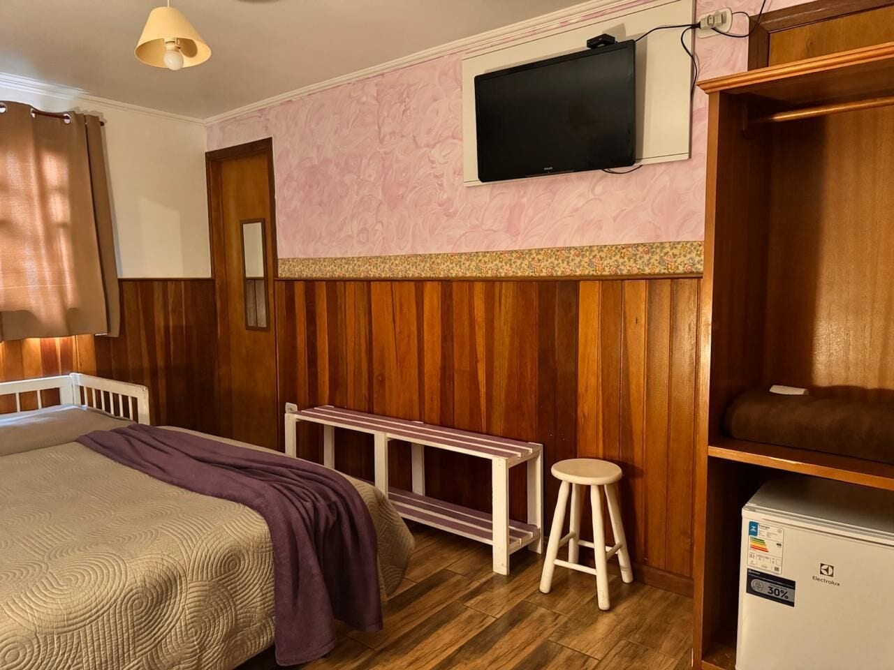 Une chambre à coucher comprenant un lit, un banc, un tabouret, une télévision et un réfrigérateur.