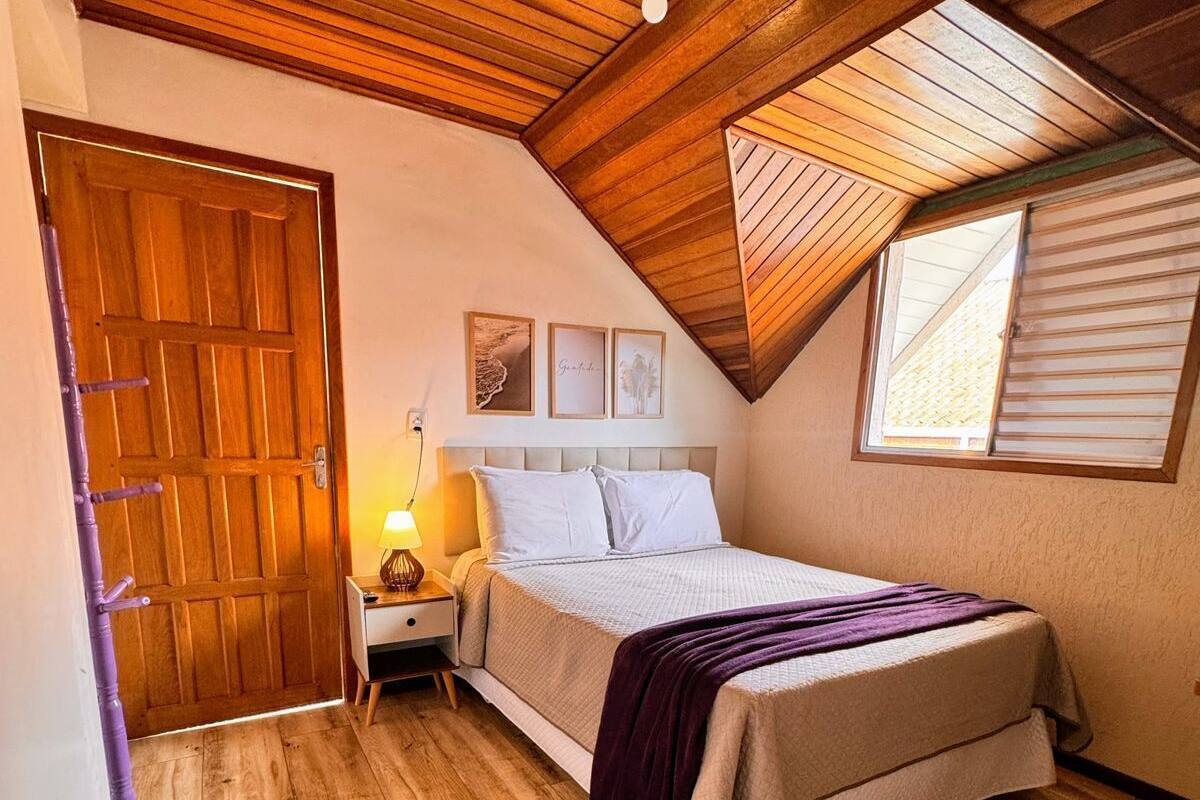 A bedroom with a wooden ceiling, a bed with a white headboard, a nightstand with a lamp, and a window with blinds.
