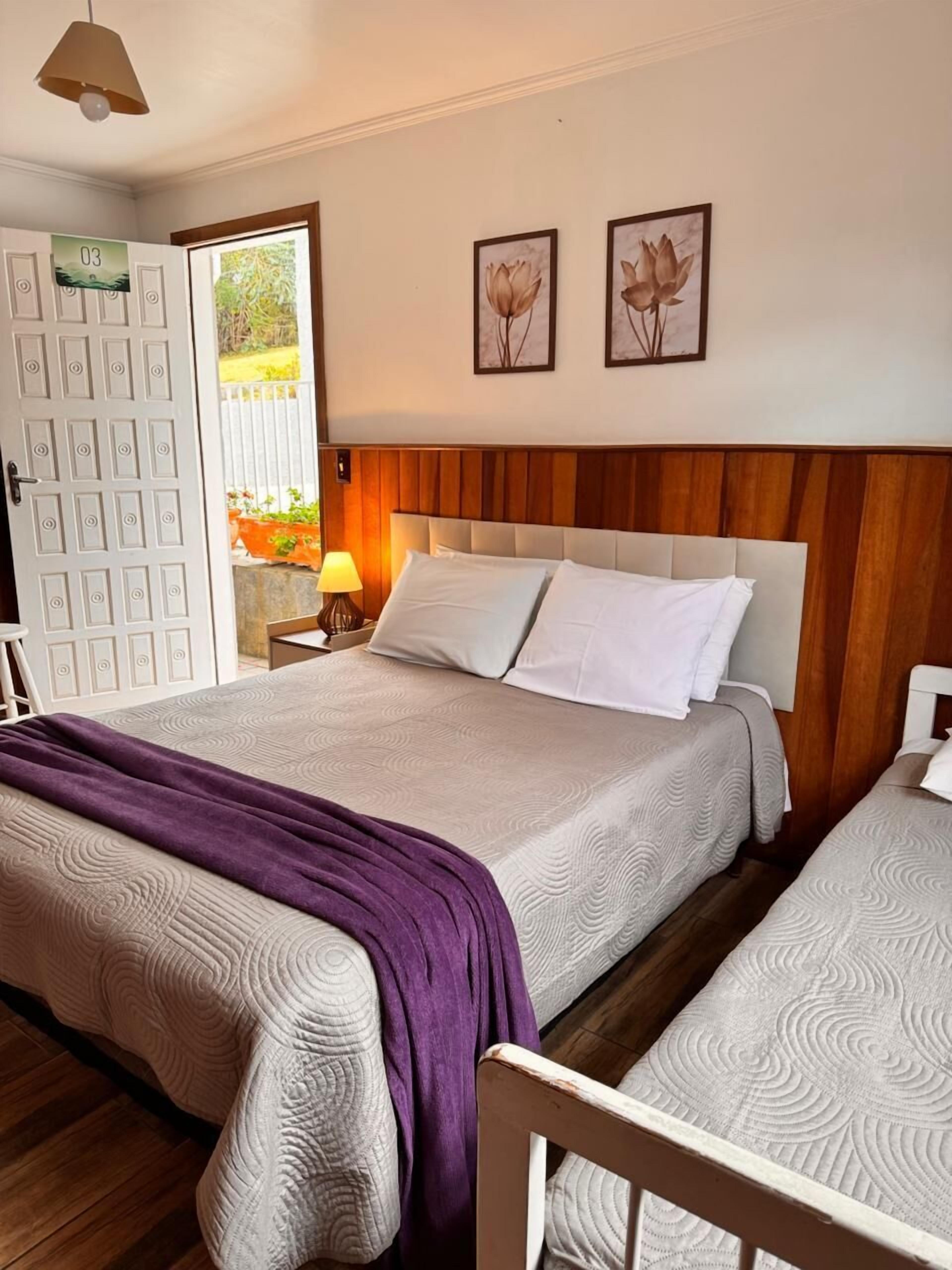 Un dormitorio con dos camas, un cabecero de madera, una puerta con un número y una ventana con vistas a la vegetación.
