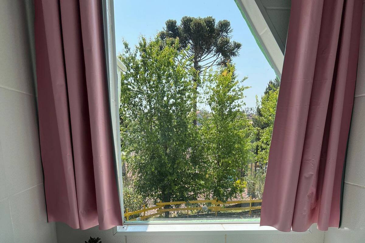 A bathroom with a bathtub, pink curtains, and a window overlooking a garden.