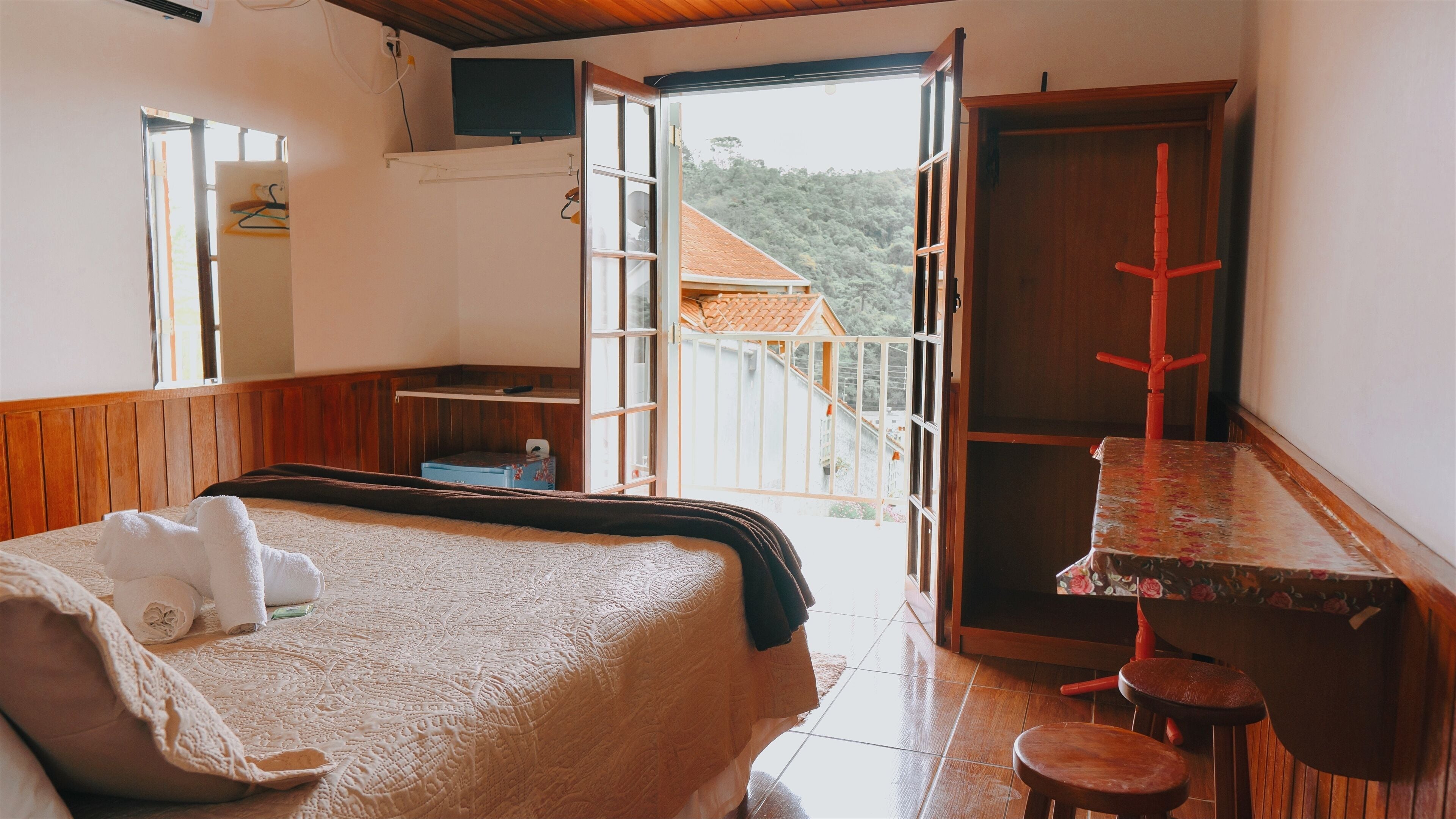 Un dormitorio con cama, una mesa y una silla. Hay una ventana y una puerta que da a un espacio exterior.