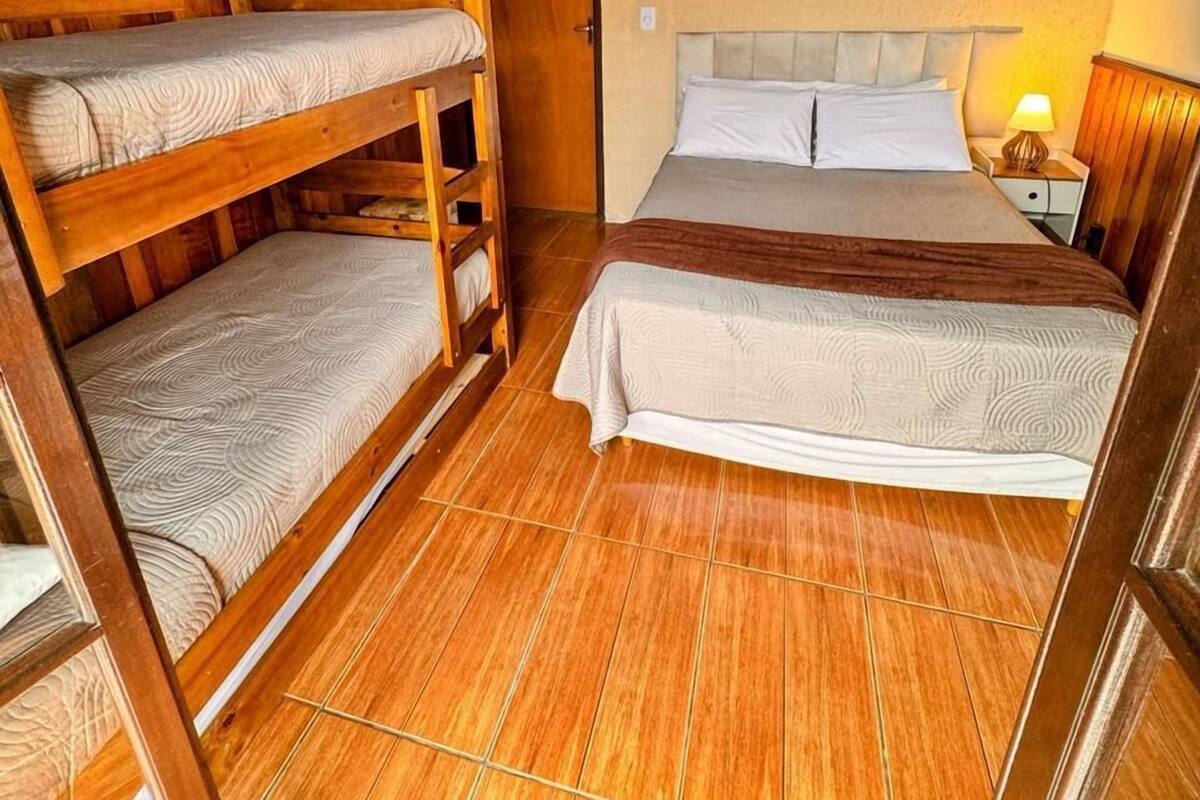 A room with bunk beds, a single bed, wooden flooring, and a ceiling light fixture.