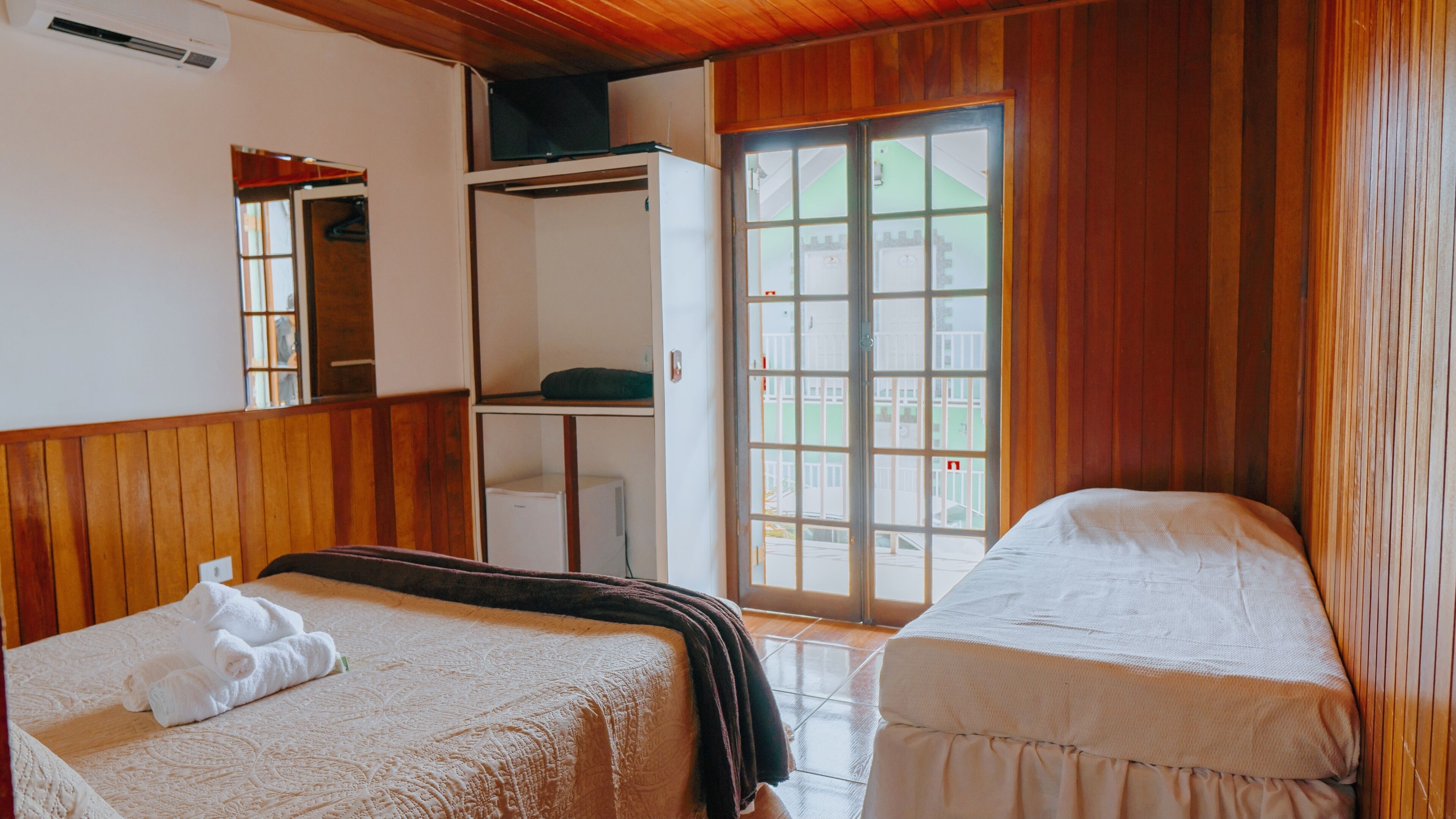 A room with two beds, a wardrobe, and a window with a view of buildings.