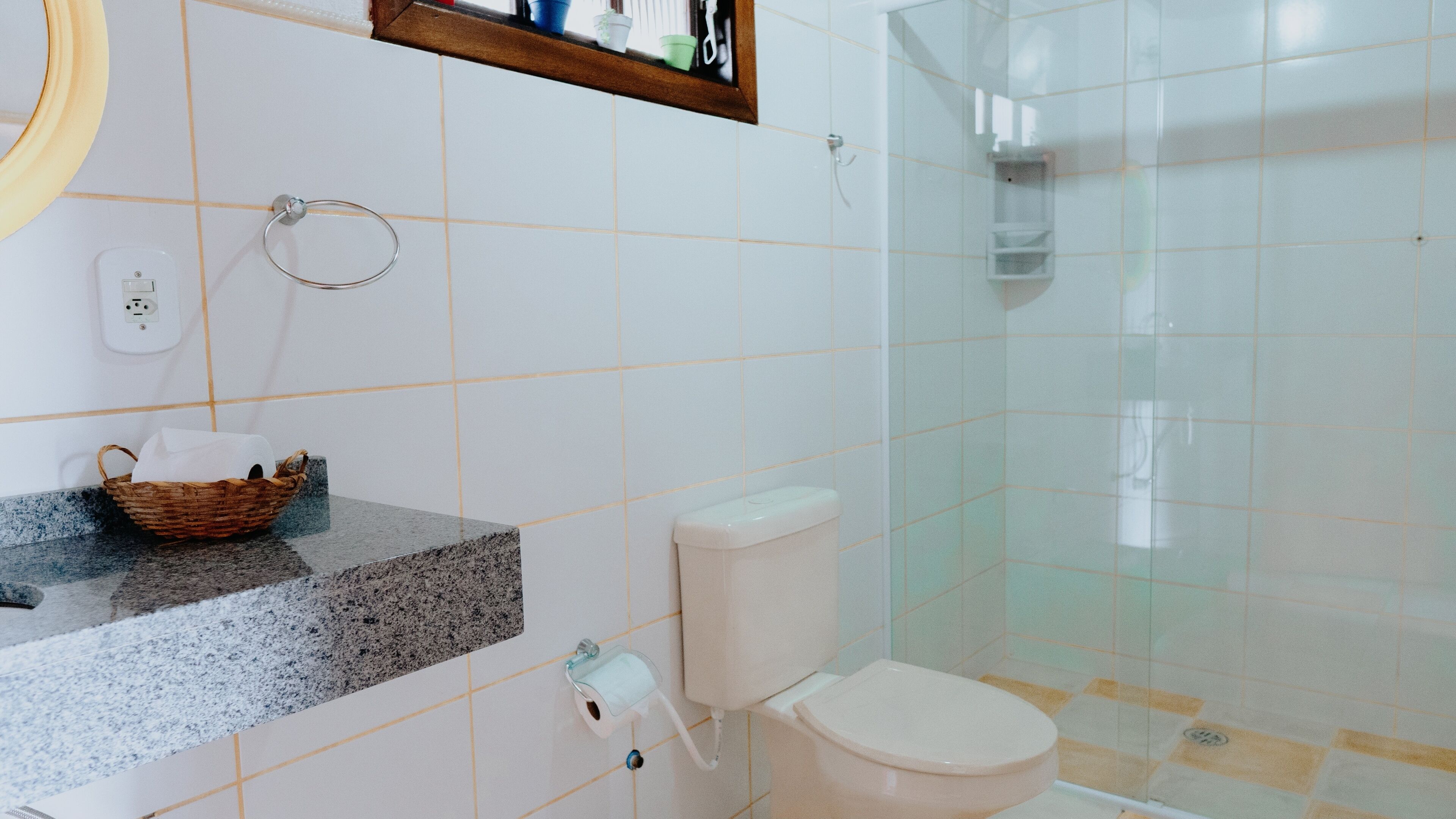 Un baño con inodoro, lavamanos con encimera de granito, una cesta y una cabina de ducha con paredes de cristal.