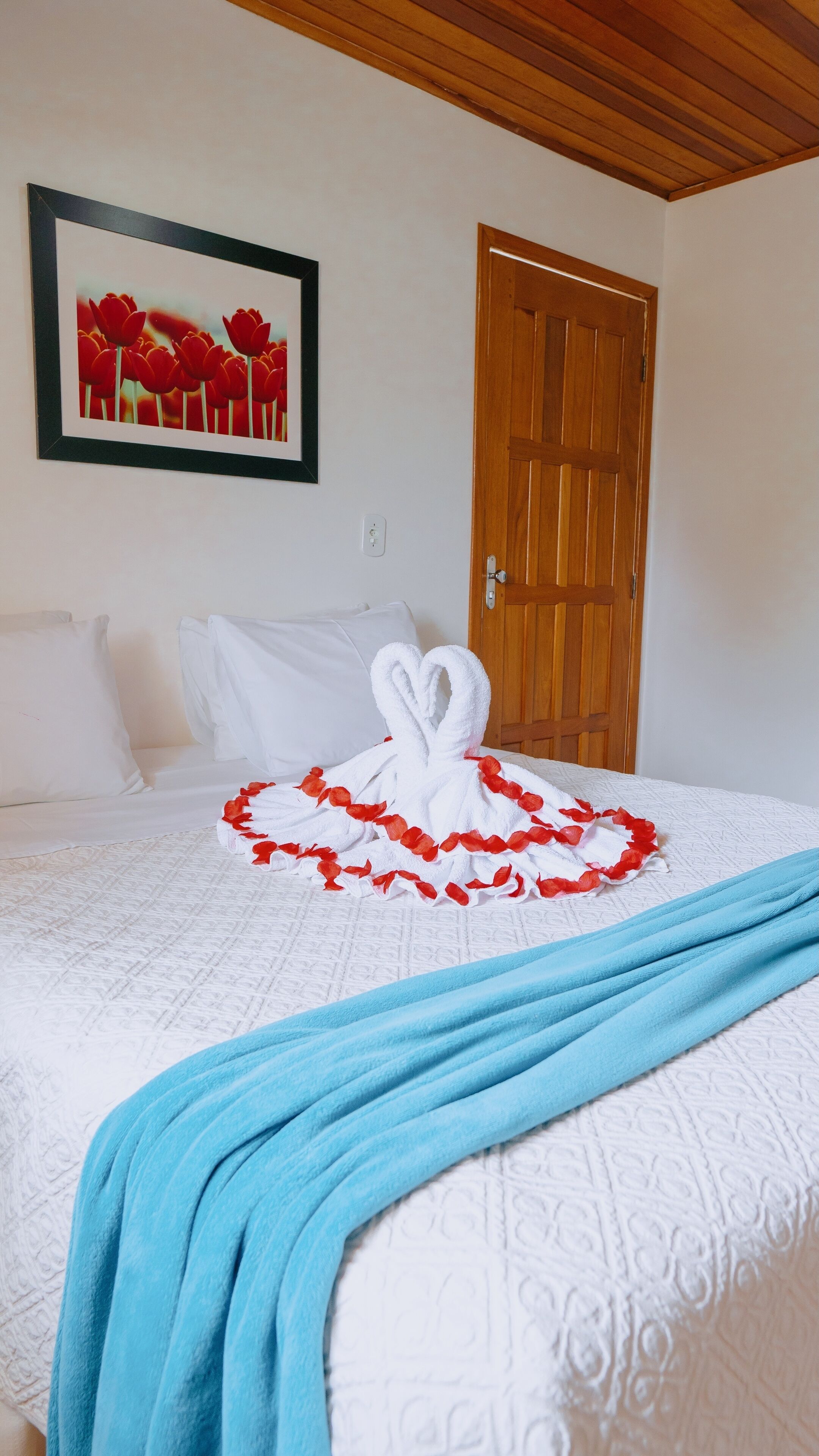 Une chambre d’hôtel avec un lit, un tableau encadré au mur, une porte en bois et une serviette pliée décorativement sur le lit.