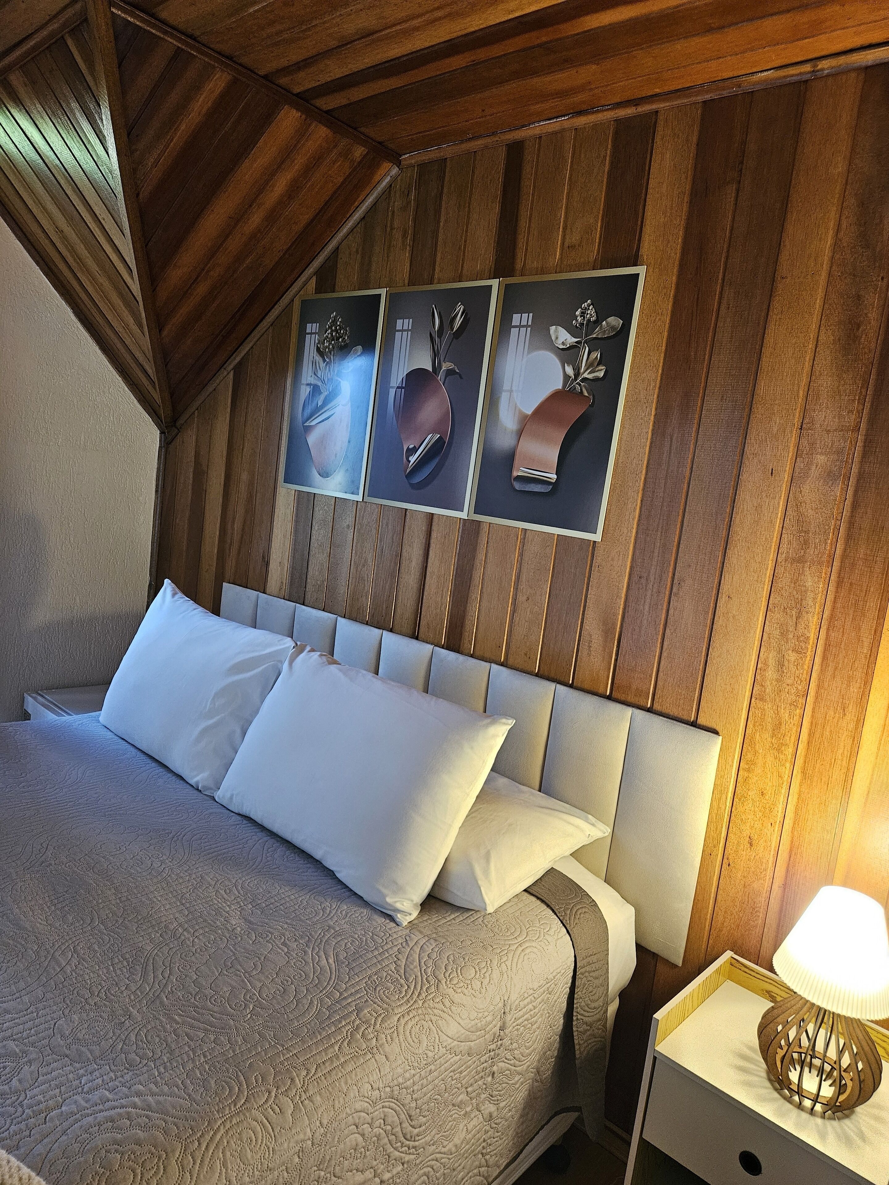 A bedroom with a wooden ceiling, a bed with white bedding, and a nightstand with a lamp.