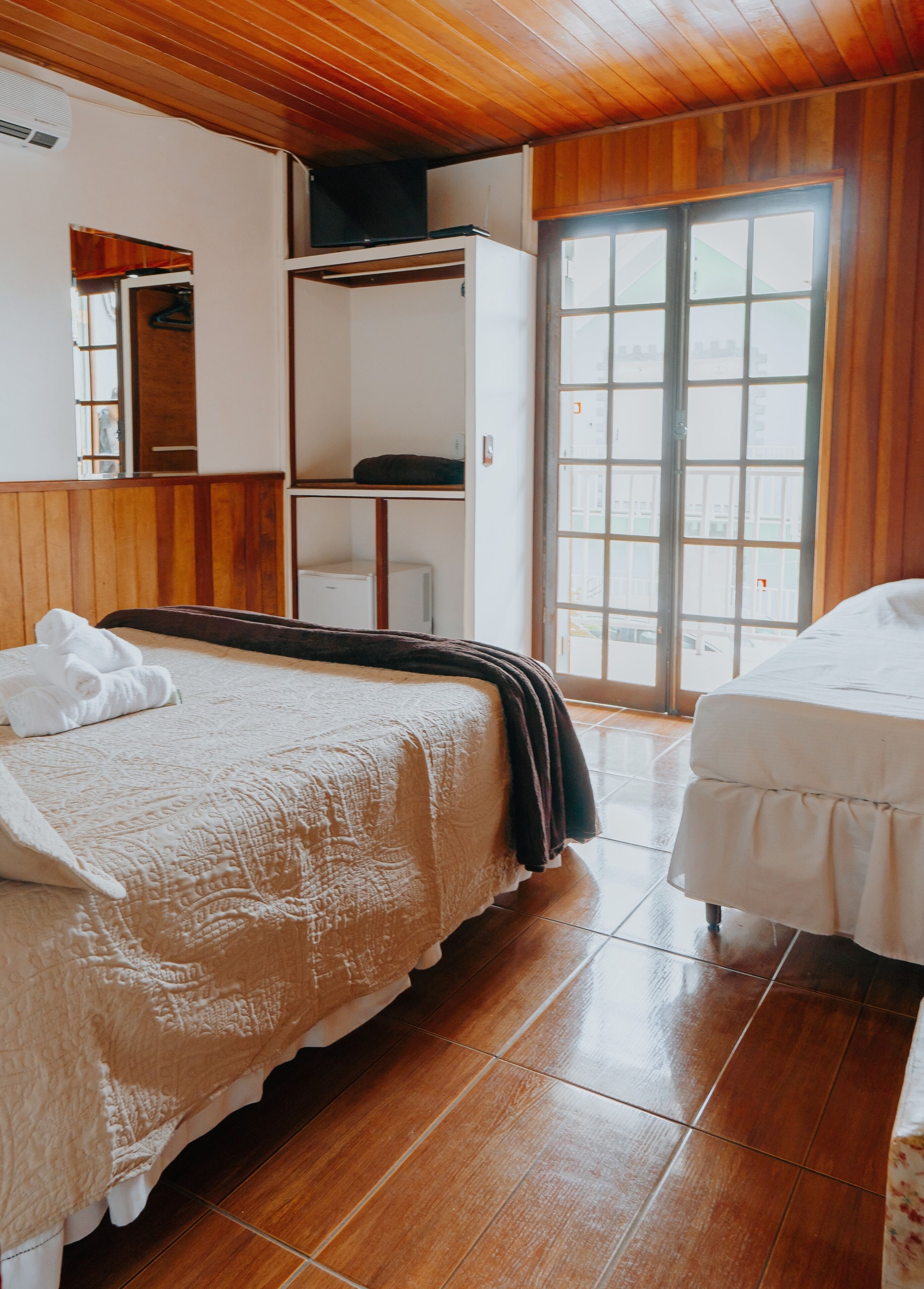 A bedroom with a large bed, a smaller bed, a wardrobe, and a sliding glass door to the outside.