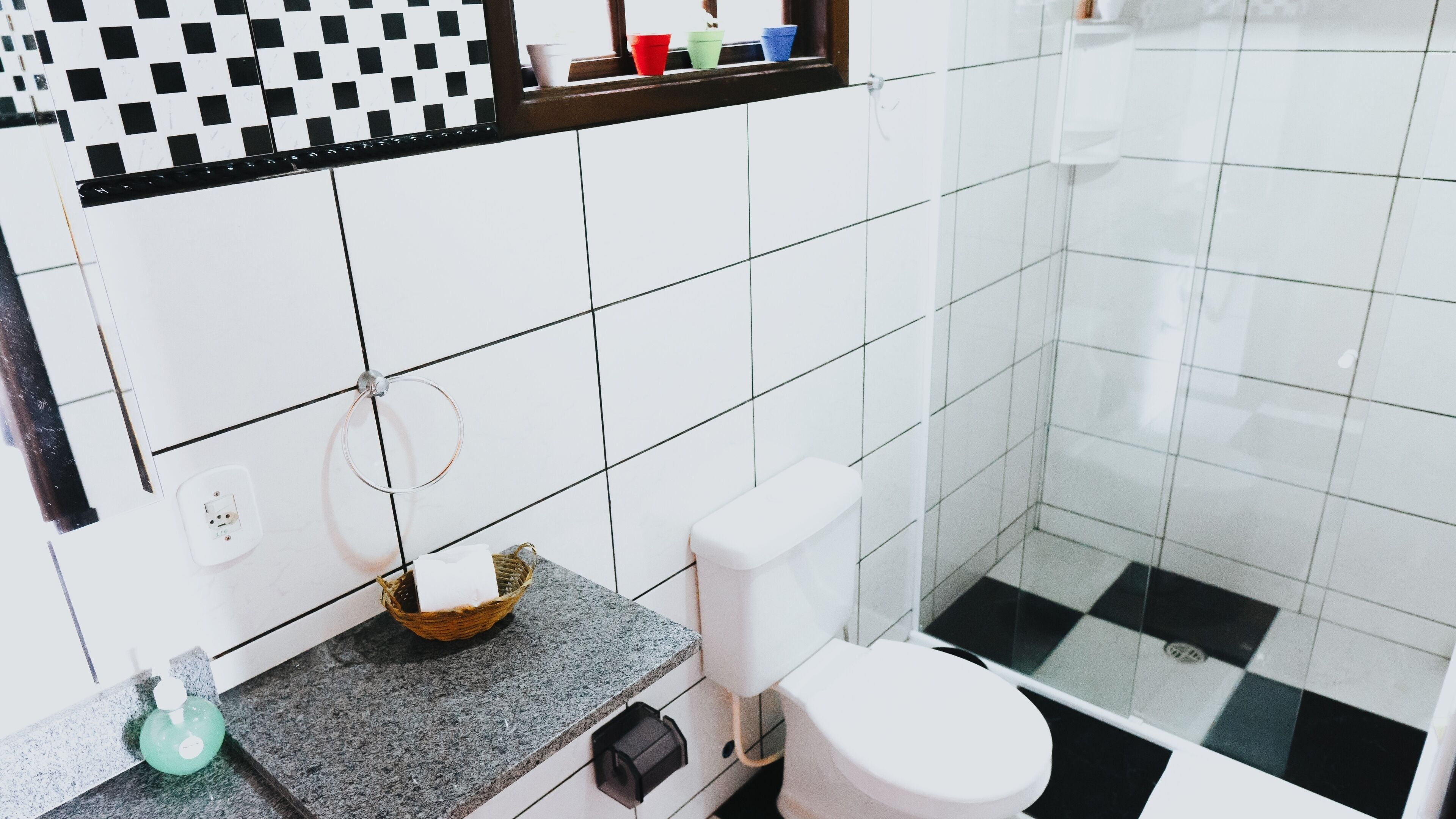 A bathroom with white tiles, a granite countertop, a toilet, and a shower area.