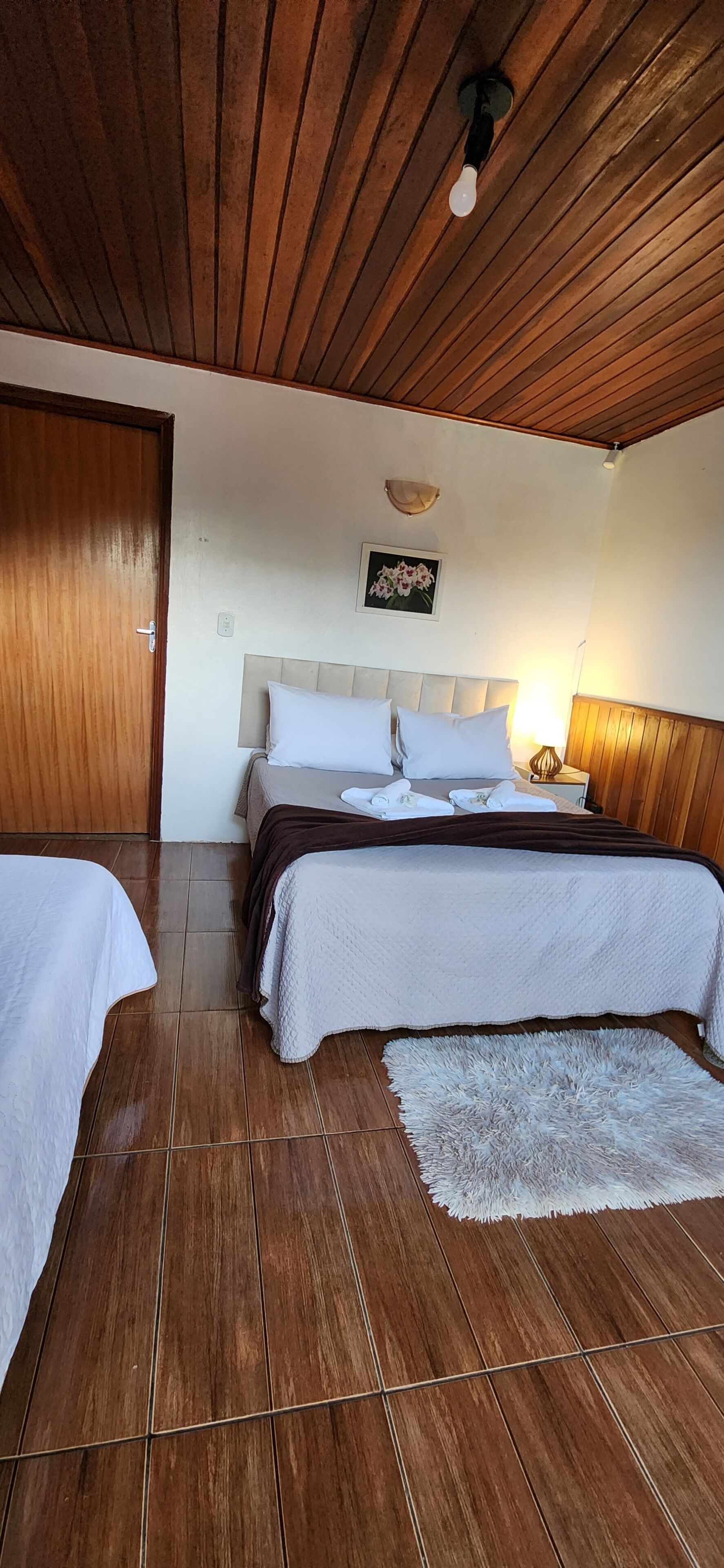 A bedroom with two beds, wooden flooring, a ceiling light, and a wall-mounted picture.