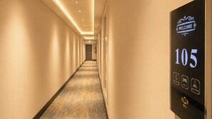Un pasillo de hotel con un letrero de bienvenida, el número de habitación 105 e iconos que representan servicios como baño, registro de entrada y una sala de desayunos.