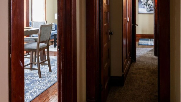 A hallway with wooden doors leading to a dining area with a table and chairs. - Two Bedroom Cutie in Midtown (Omaha)