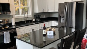 A modern kitchen with white cabinets, a stainless steel refrigerator, a built-in island with bar stools, and a pendant light fixture. - Cozy private getaway built for couples to reconnect !!  (West Union)