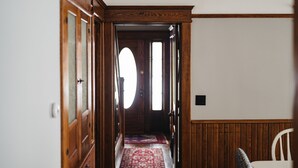 A hallway with wooden doors, a red patterned rug, and a white chair. - 4BDR Broomhead Farmhouse Main House (Williamsburg)