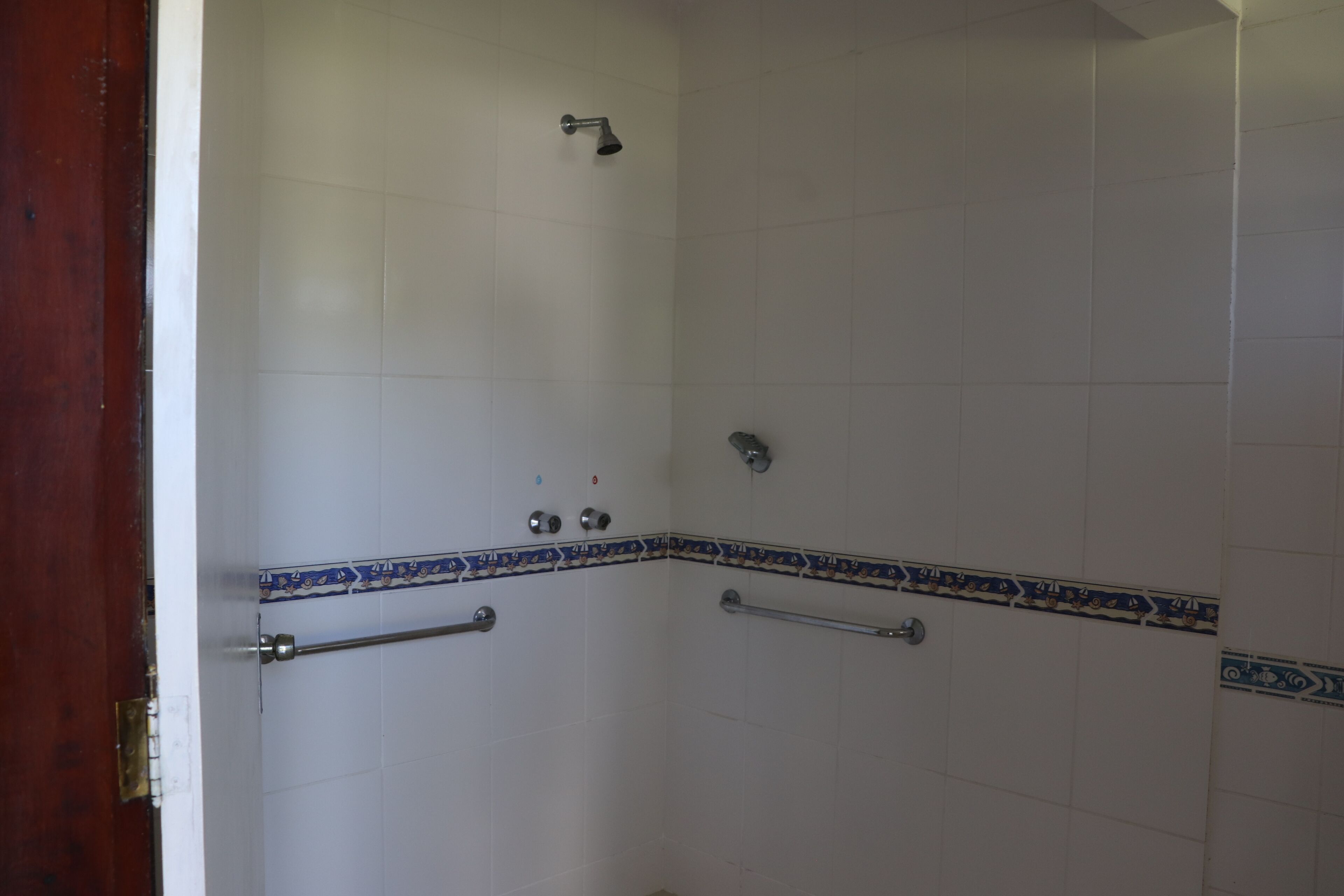 A shower with white tiles and blue decorative borders.