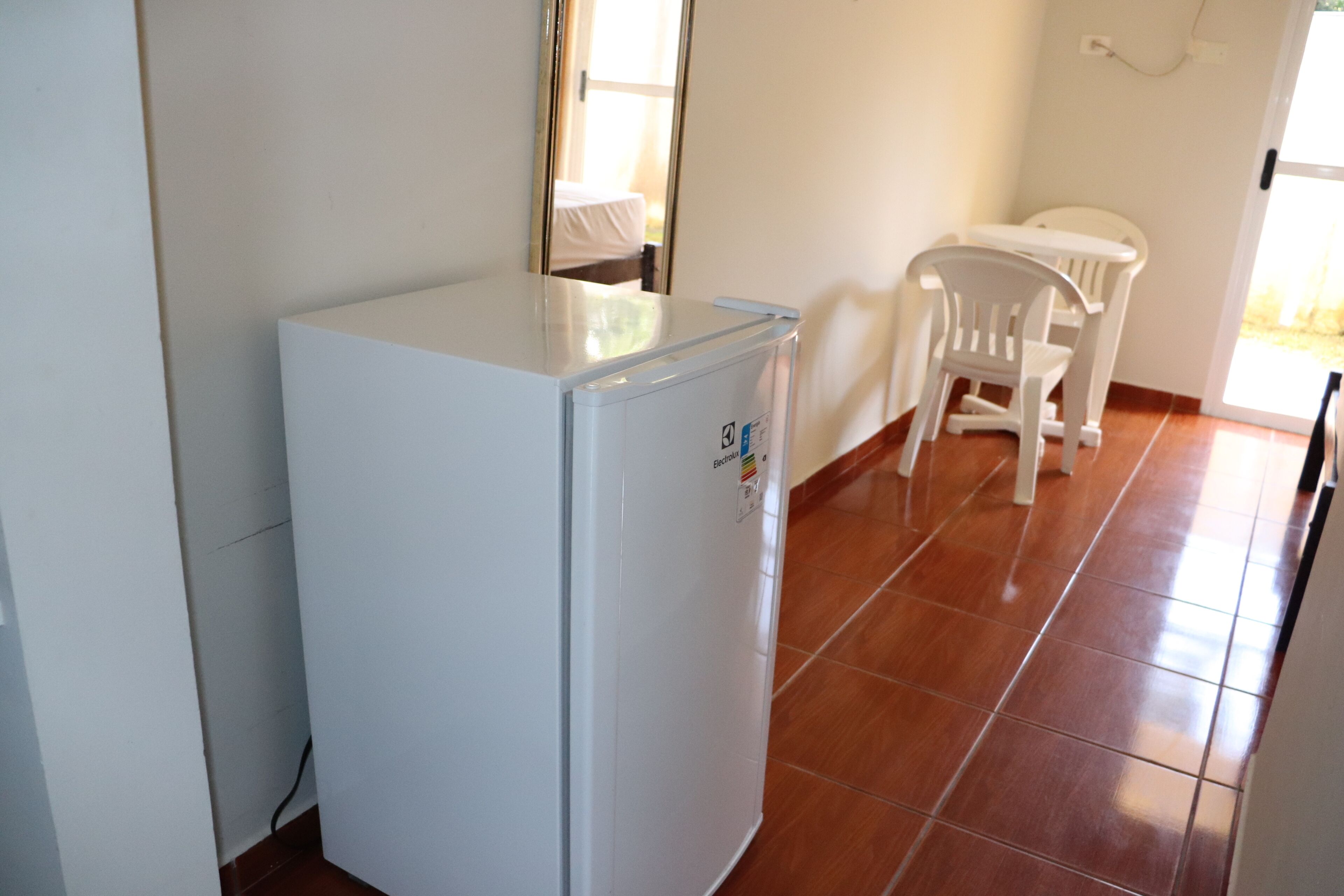 Una stanza compatta con un frigorifero bianco, un tavolino bianco e una sedia bianca.