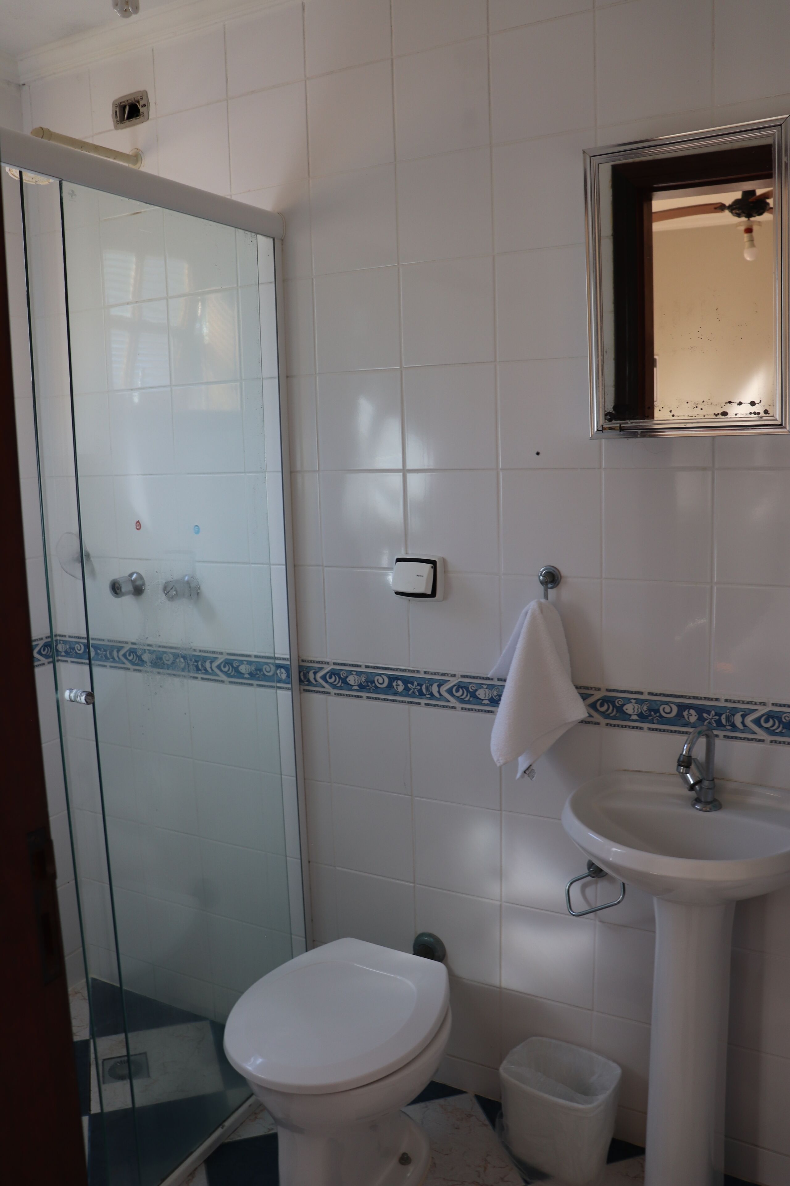 Une salle de bain avec une douche à parois de verre, des toilettes blanches, un lavabo et une serviette accrochée au mur.