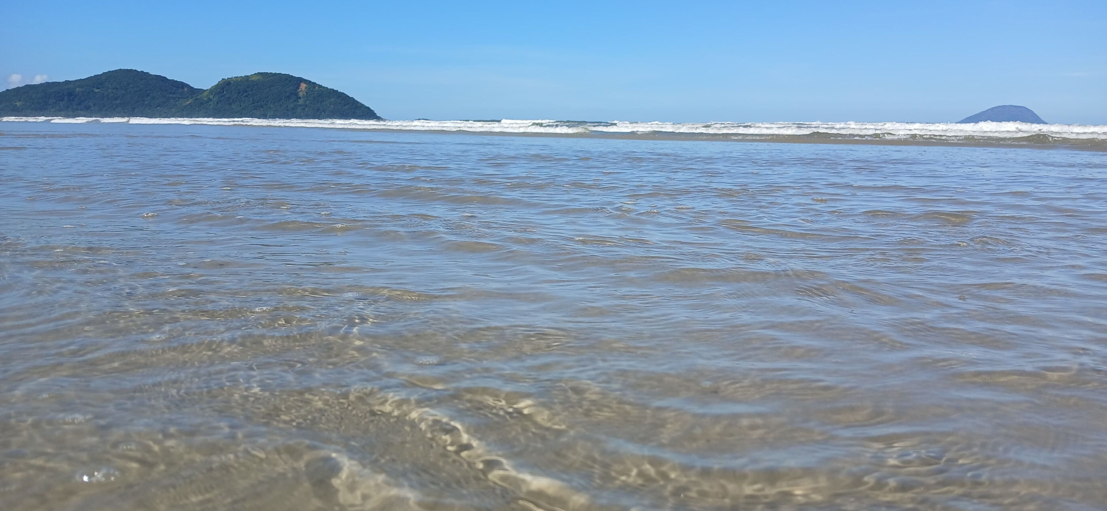 Una playa con agua cristalina y islas a lo lejos.