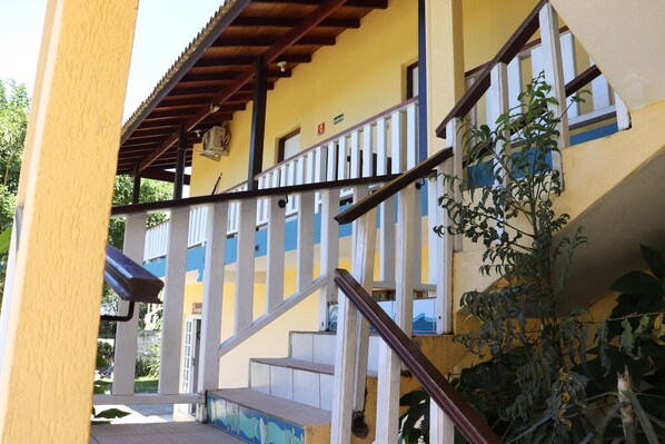 A yellow building with white railings and a staircase leading to the upper floor.