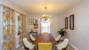 A dining room with a wooden table, white upholstered chairs, a chandelier, and a window with curtains. - Music City House, 4 miles to BDWY, Free Parking (Nashville)