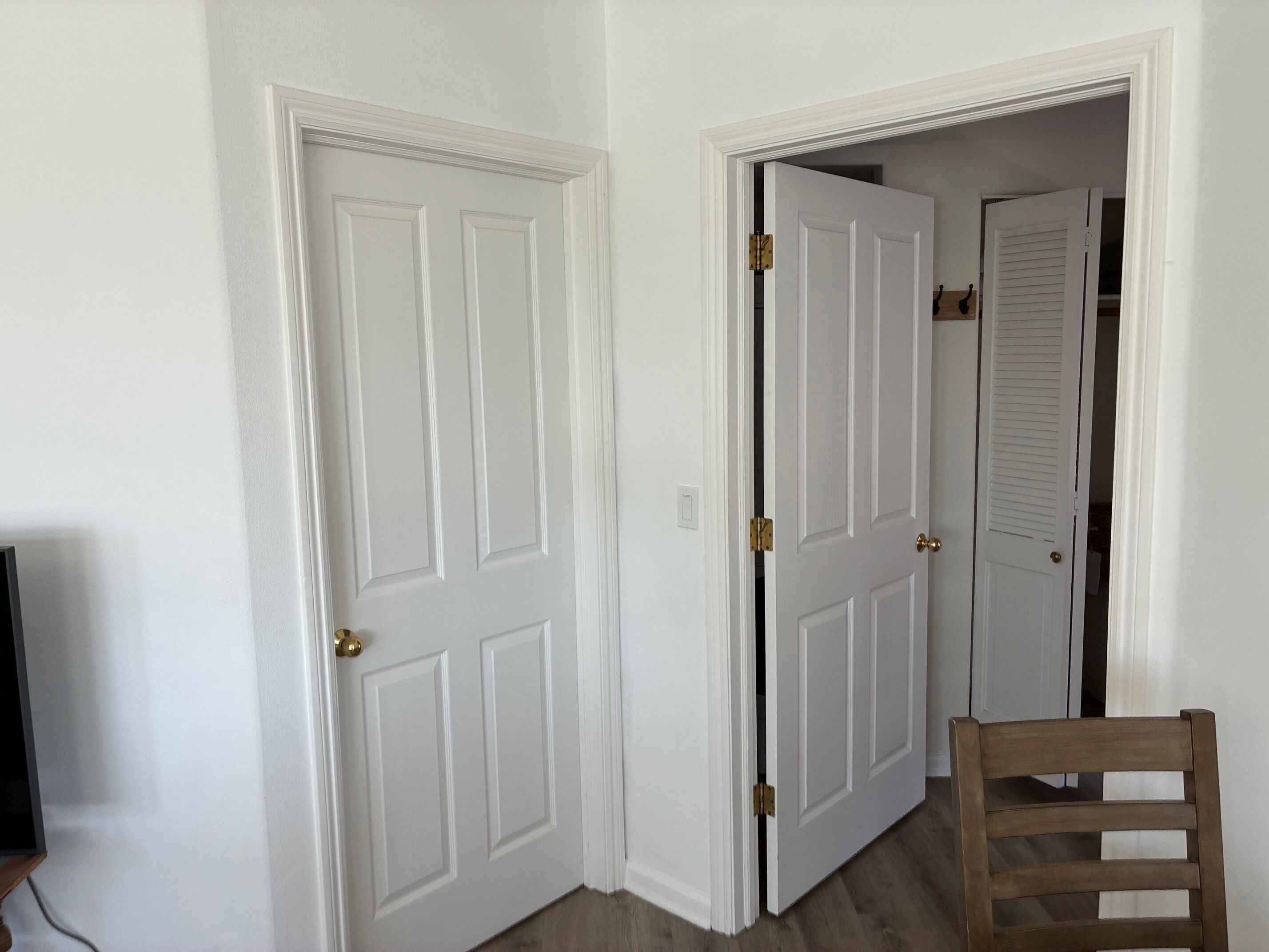 A hallway with white doors, a wooden chair, and a television.