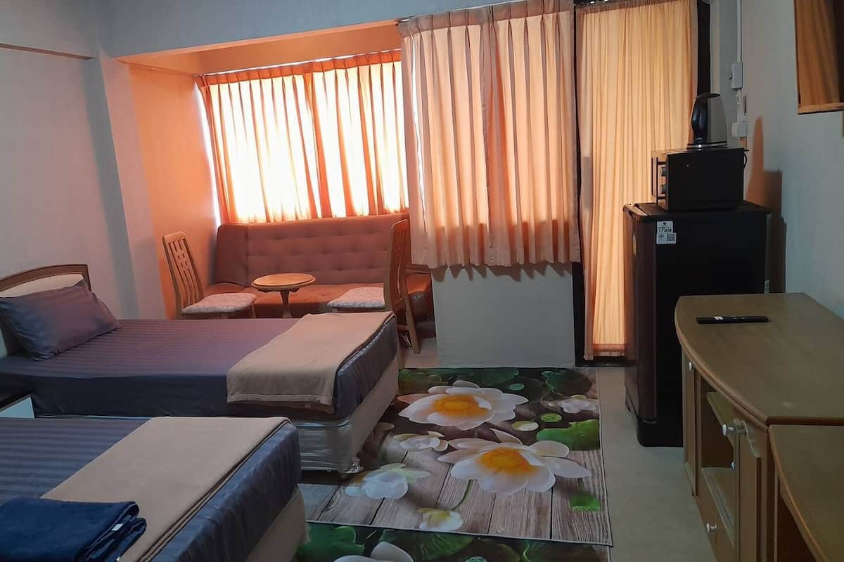 A compact hotel room with two single beds, a small sofa, a table, and a TV.