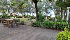 A paved outdoor area with a wooden table and chairs, surrounded by greenery and trees. - Victory View Rayong Beach (Rayong)