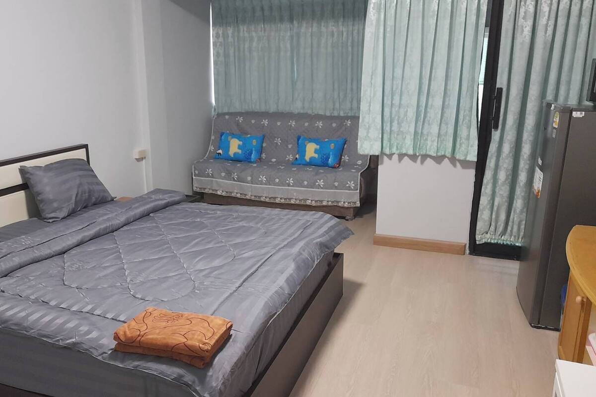 A bedroom with a bed, a sofa, a TV, and a refrigerator.