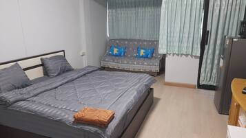 Un dormitorio con cama, sofá, televisión y refrigerador.