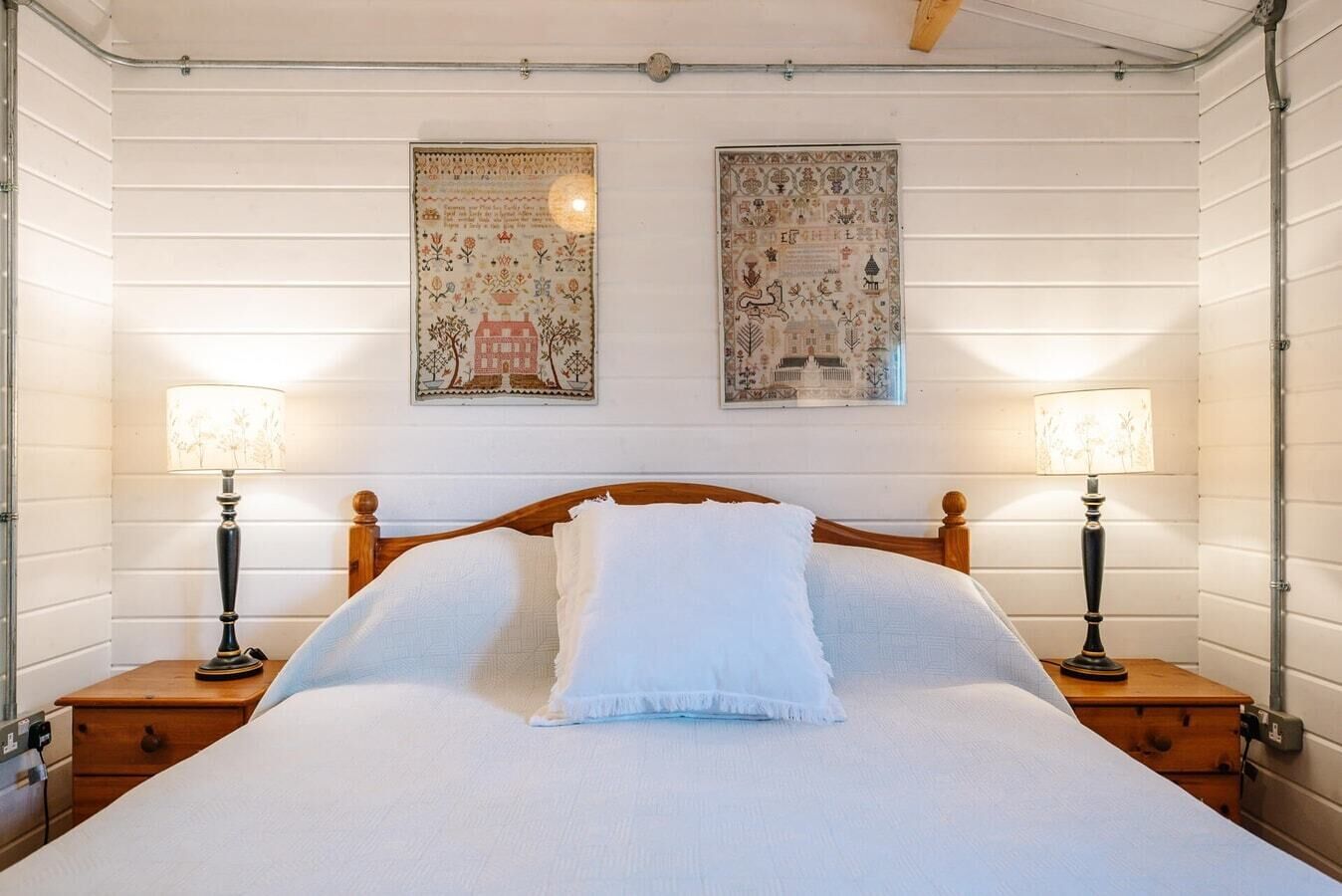 Un lit bien fait, avec du linge de lit blanc, deux tables de chevet avec des lampes et deux tableaux encadrés accrochés au mur.