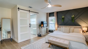 Un dormitorio con cama, ventilador de techo, televisor y puerta corrediza.