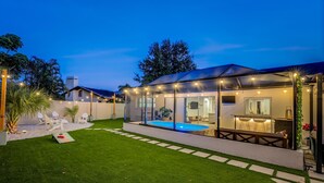 Una casa moderna con piscina, zona de estar exterior cubierta y césped bien cuidado.