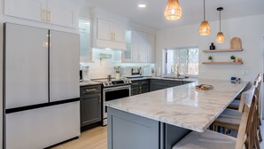 Una cocina moderna con armarios blancos, una isla de mármol e iluminación colgante.
