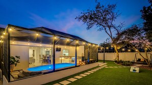 Una casa moderna con piscina cubierta, un patio y un césped bien cuidado.