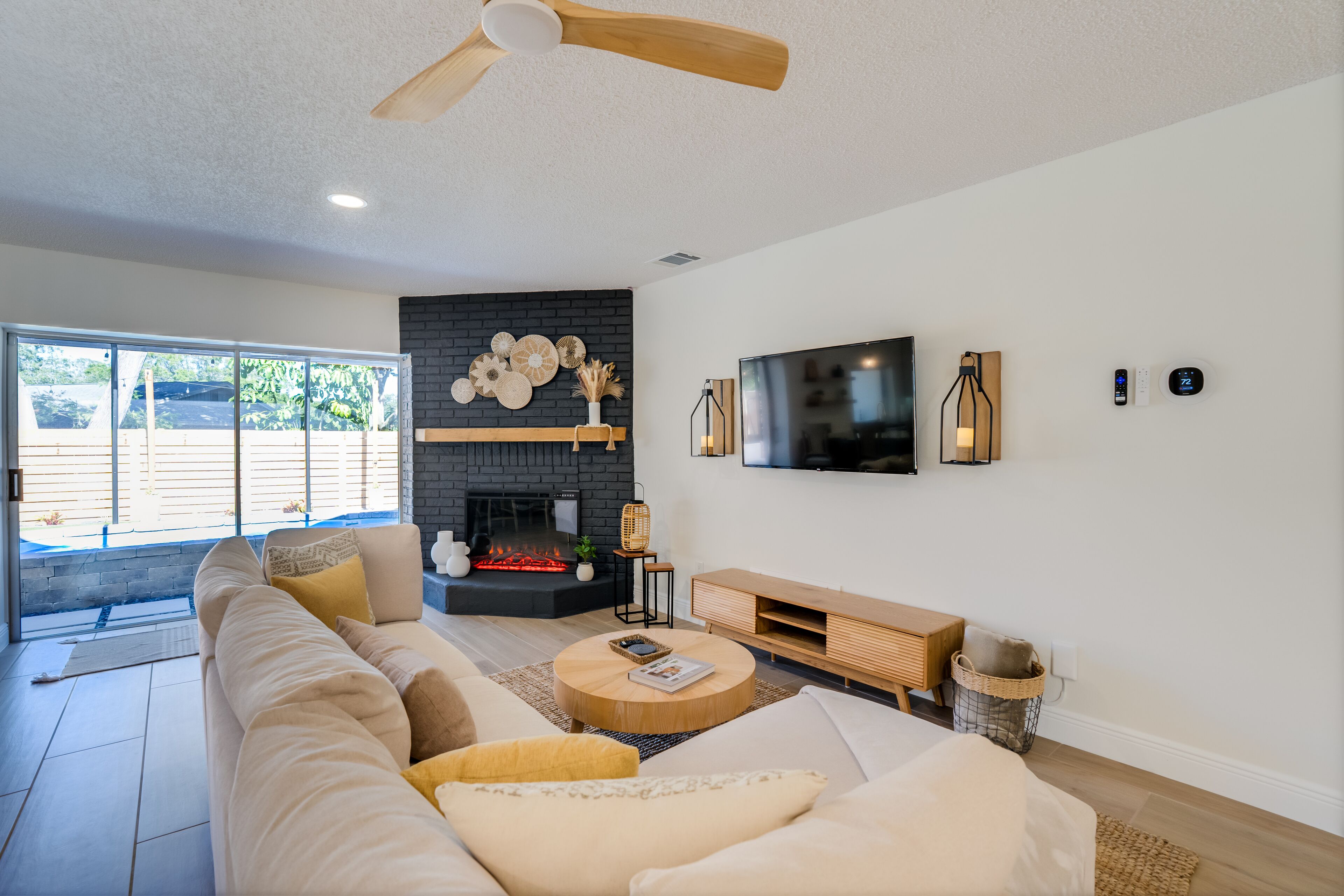 A modern living room with a large sofa, a fireplace, a flat-screen TV, and a ceiling fan.