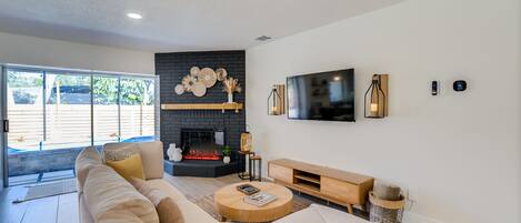 A modern living room with a large sofa, a fireplace, a flat-screen TV, and a ceiling fan.
