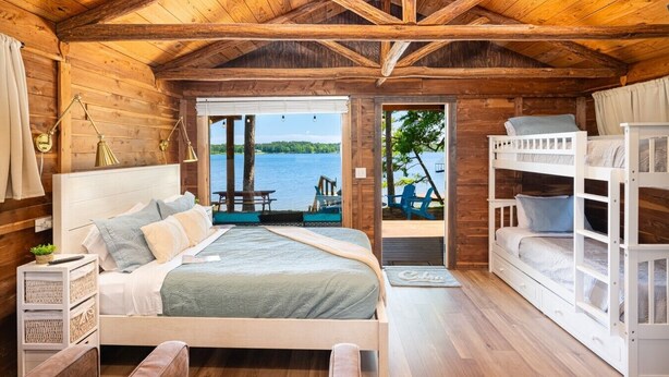 A cabin with a wooden interior, a bed, a bunk bed, and a view of a lake. - Rustic Cedar Waterfront Cabin 8 on Toledo Bend (Hemphill)