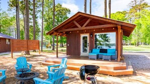 A covered outdoor seating area with a grill, blue Adirondack chairs, and a fire pit. - Rustic Cedar Waterfront Cabin 8 on Toledo Bend (Hemphill)