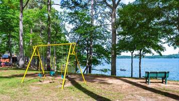 A park with a swing set, a bench, and a lake view.