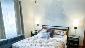 Ett hotellrum med en säng, två sängbord, en väggmonterad lampa och ett fönster med gardiner.