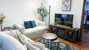 Ett vardagsrum med en soffa, en tv placerad på ett träskåp, ett litet runt bord och en golvlampa.
