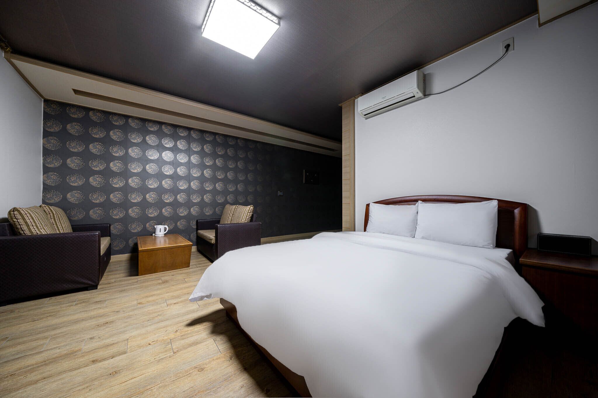 A hotel room with a large bed, two armchairs, a wooden coffee table, and a patterned wallpaper.