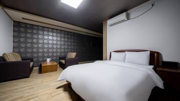 A hotel room with a large bed, two armchairs, a wooden coffee table, and a patterned wallpaper.
