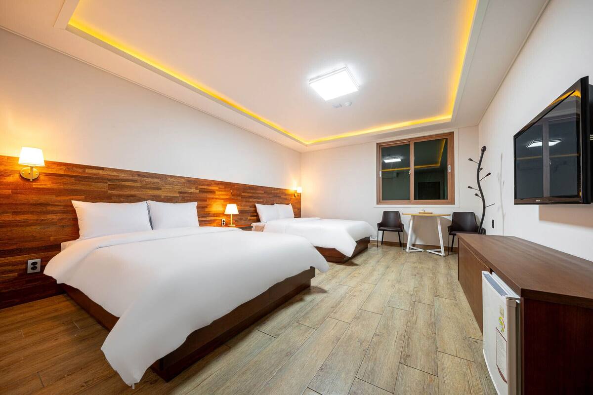 A hotel room with two beds, a desk, chairs, a TV, and a wooden accent wall.