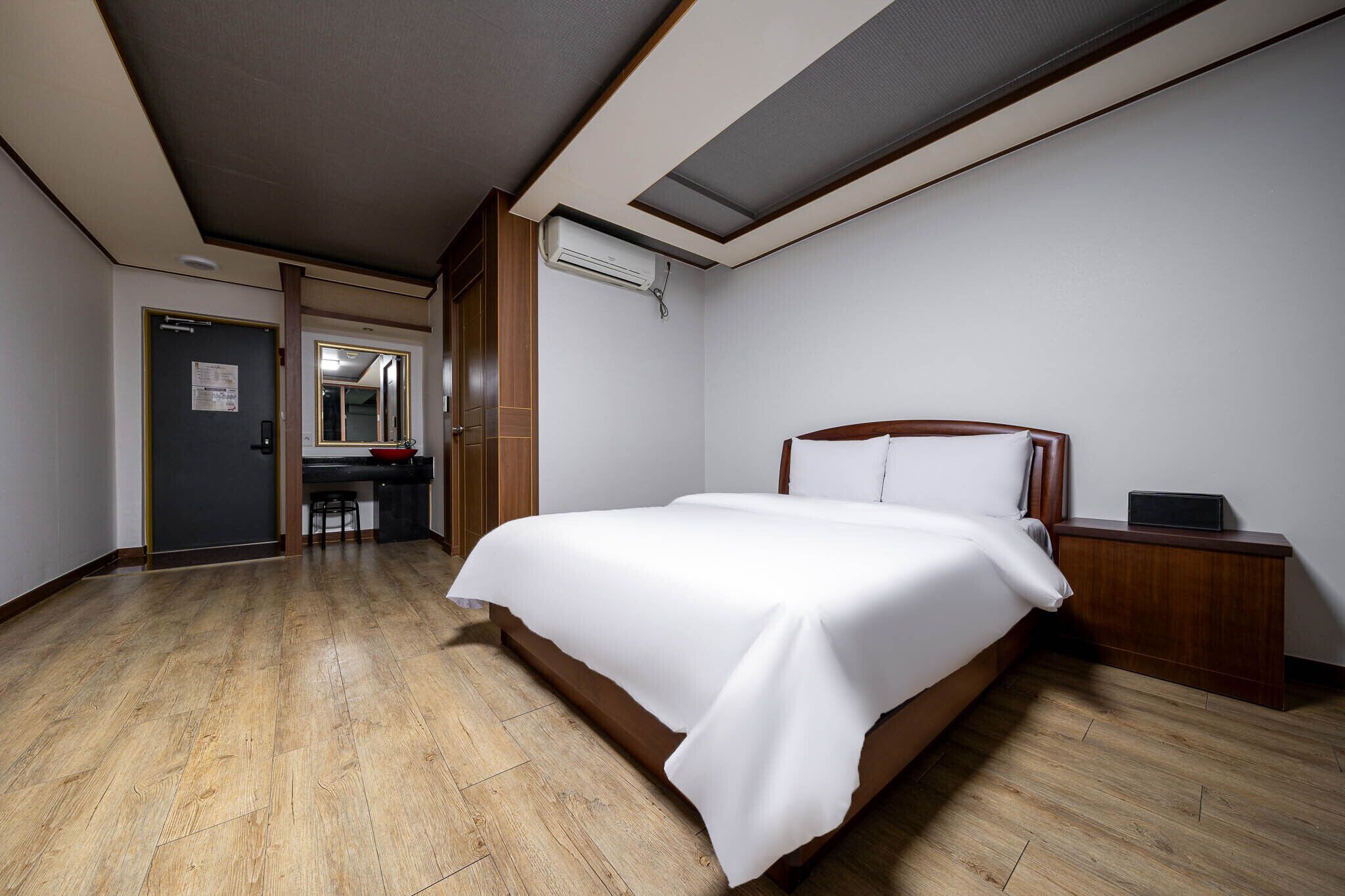 A hotel room with a large bed, a wooden nightstand, a desk with a chair, and a mirror.