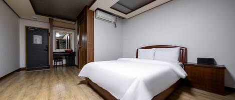 A hotel room with a large bed, a wooden nightstand, a desk with a chair, and a mirror.