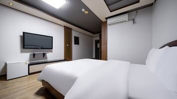 Habitación de hotel moderna con una cama grande, un televisor de pantalla plana montado en la pared, un refrigerador pequeño y un equipo de aire acondicionado instalado en el techo.