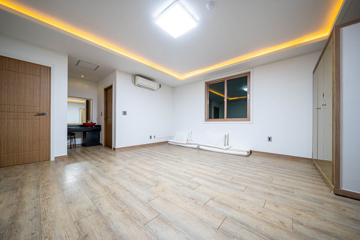 A spacious room with wooden flooring, a large window, and a ceiling light.