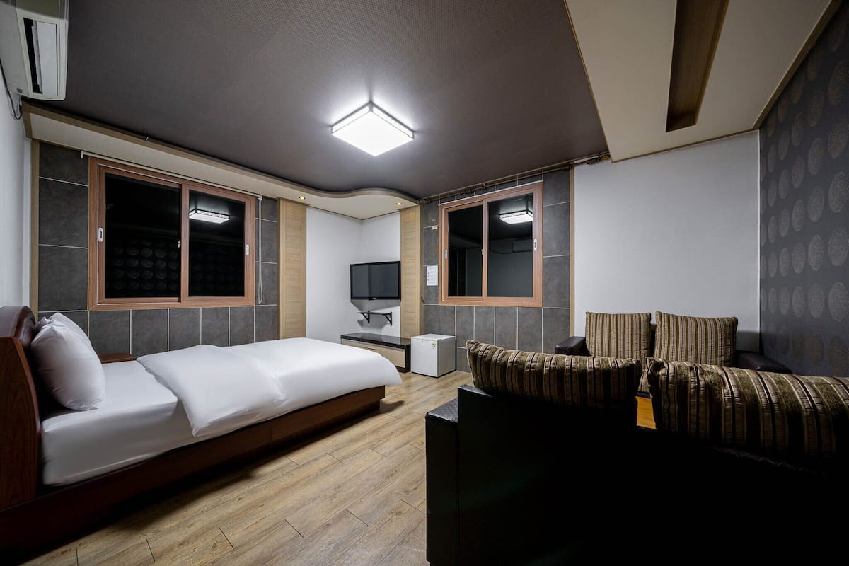 A modern hotel room with a large bed, a sofa, a TV, and a small desk.