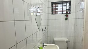 A small, tiled bathroom with a white sink, toilet, and a window with bars. - Tamernique Apartments (St. George's)