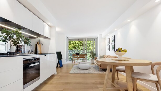 A modern kitchen with white cabinetry, a built-in oven, and a dining area with a round wooden table and chairs. - Studio 221 on Bondi Beach (Bondi)